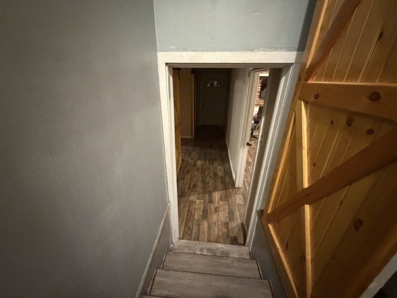 A narrow stairway leading to a room with a wooden floor and a door with a wooden frame.