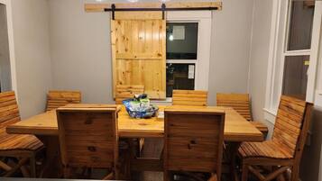 A dining area with a wooden table and chairs, a hanging light fixture, and a window.