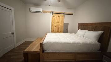 A bedroom with a wooden bed, a ceiling fan, an air conditioning unit, and a wooden nightstand.