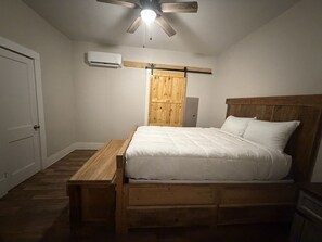 A bedroom with a wooden bed, a ceiling fan, an air conditioning unit, and a wooden nightstand. - Messick Farmstyle Home (Marksville)