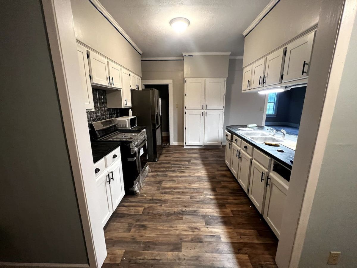 A narrow kitchen with white cabinets, a black stove, and a wooden floor.