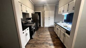 A narrow kitchen with white cabinets, a black stove, and a wooden floor.