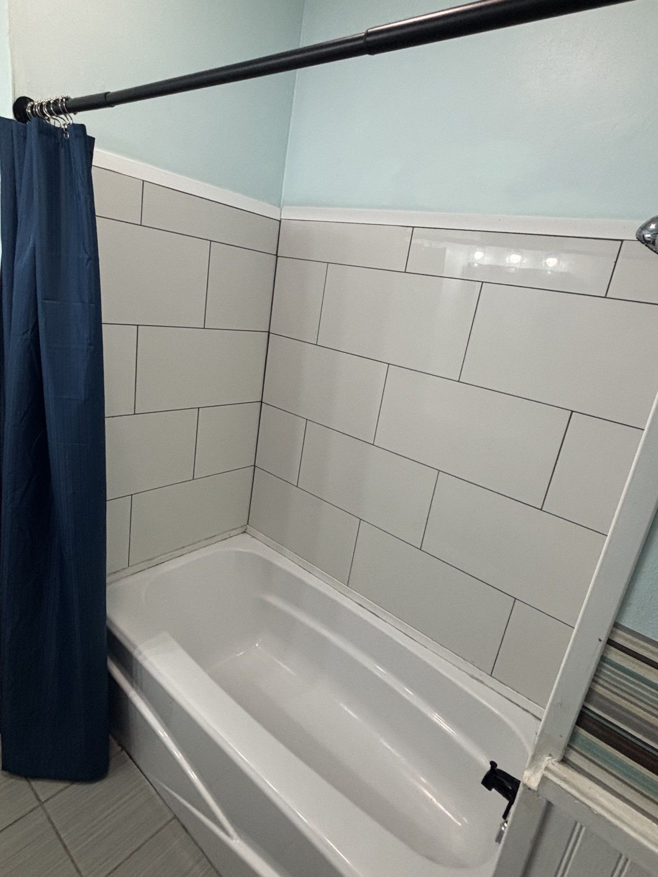 A bathroom with a white bathtub, a shower curtain, and tiled walls.