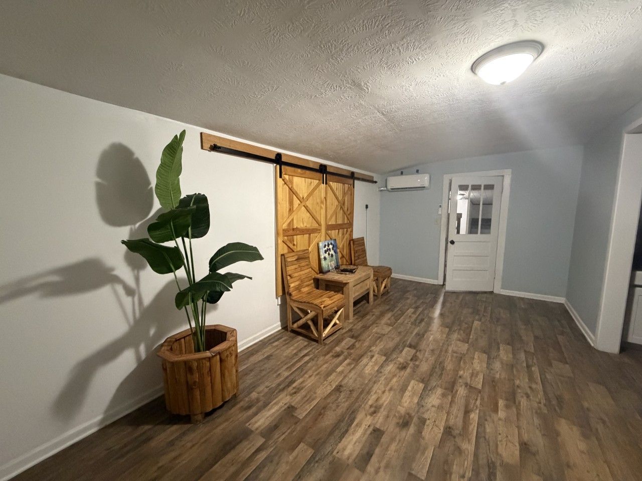 A room with wooden flooring, a sliding barn door, a potted plant, and a small table with chairs.