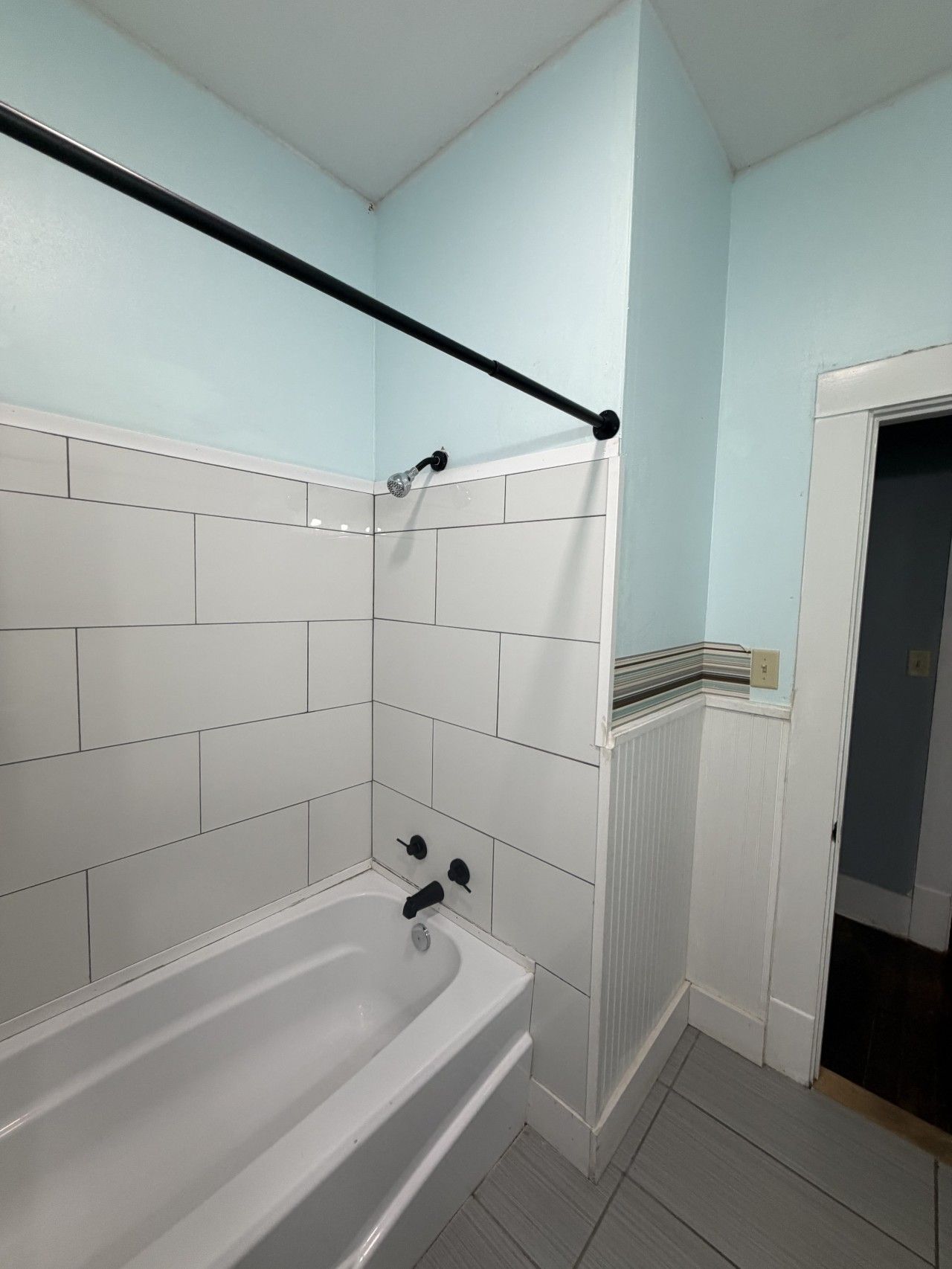 A bathroom with a white bathtub, a black towel rack, and a light blue wall.