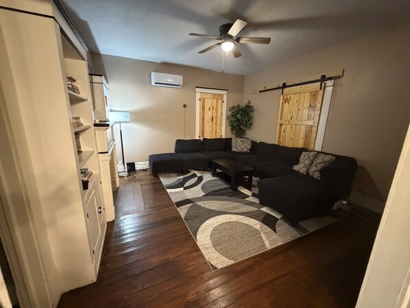 A living room with a sectional sofa, a ceiling fan, and a wooden floor.