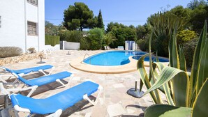 En swimmingpool med blå liggestole, en stenterrasse og en hvid bygning med et vindue.