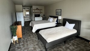 A hotel room with two beds, a kitchenette, a small seating area, and a potted plant.