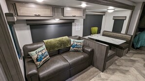 A compact RV interior with a sofa, two pillows, a small table, and cabinets.