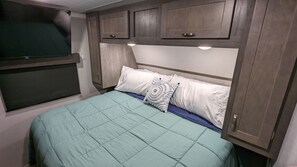 A bedroom with a bed, pillows, a TV, and wooden cabinets. - Cozy RV with 1 King bedroom, WiFi & AC in Pleasant Acworth (Acworth)