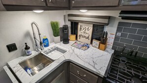 A kitchen with a sink, coffee maker, and a sign that says "Rise and Grind".