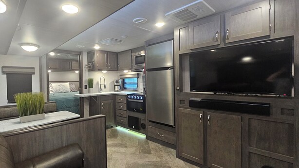 A modern RV kitchen with built-in appliances, a dining area, and a large TV.