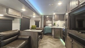 A compact RV interior with a kitchenette, a seating area, and a television.