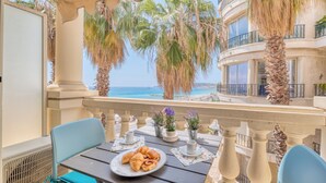 Un balcón con mesa lista para el desayuno, con vista a una playa y palmeras.