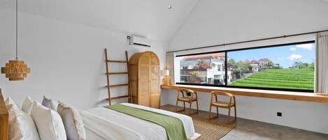 Un dormitorio con cama, escritorio, dos sillas, un amplio ventanal con vista a un campo verde y una lámpara colgante.