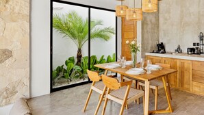 Een moderne eetruimte met een houten tafel voor vier personen, omringd door rieten stoelen. Een groot raam biedt uitzicht op weelderige begroeiing.