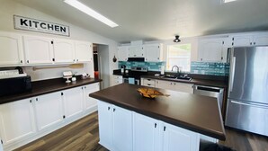 A modern kitchen with white cabinets, a central island, a stainless steel refrigerator, and a ceiling light fixture.