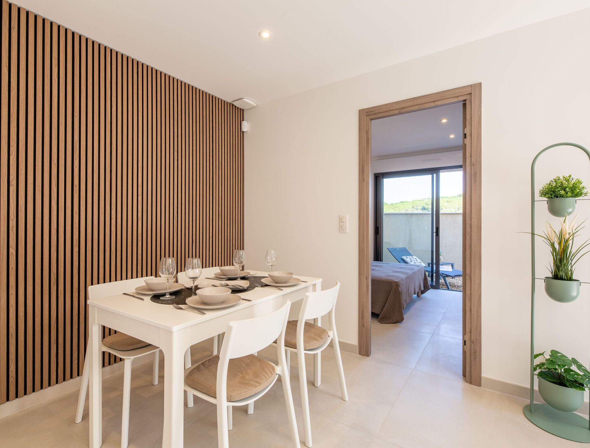 Un comedor con una mesa blanca dispuesta para seis personas, sillas blancas y un panel de madera con listones.