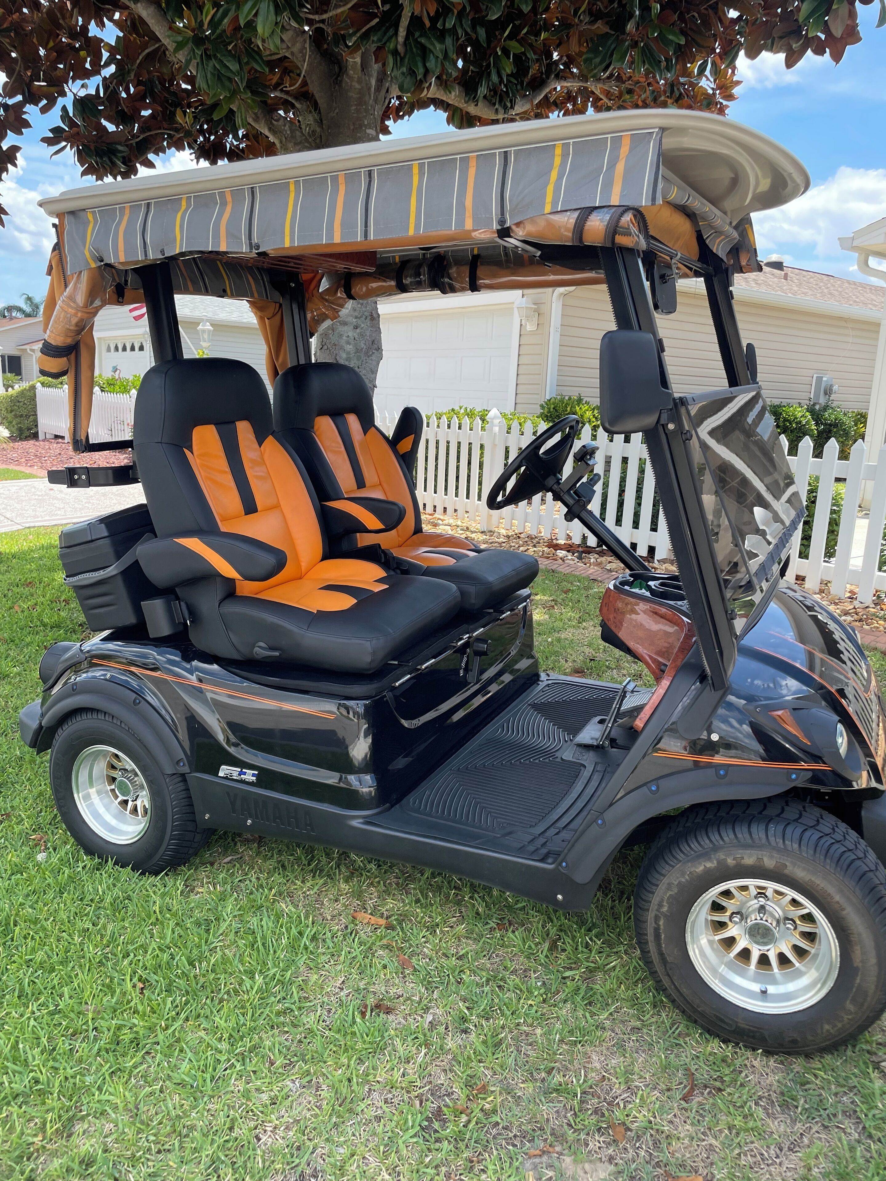 Um carrinho de golfe com bancos laranja e preto, um volante e um toldo.