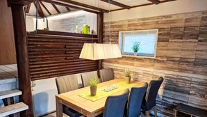 Un coin repas chaleureux avec une table en bois, des chaises et une lampe. Une fenêtre avec une plante est visible sur le mur.