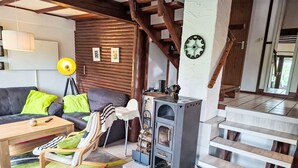 Un salon chaleureux avec un canapé, une table en bois, un transat pour bébé, une cheminée et un escalier.