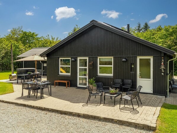 Un bâtiment noir doté d’un patio, d’un espace extérieur aménagé avec des sièges et d’un barbecue.