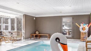 Une piscine avec un flotteur en forme de cygne, des meubles en bois et de grandes fenêtres.