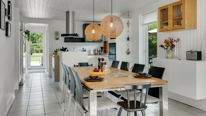 Une cuisine moderne avec un coin repas, comprenant une grande table en bois, des chaises et des luminaires suspendus.