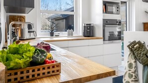 Une cuisine moderne avec un plan de travail en bois, un évier, une fenêtre donnant sur une maison et un four à micro-ondes.