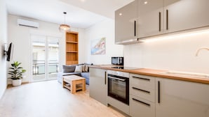 Een moderne keuken met een ingebouwde oven, een houten aanrecht en een spoelbak. Er is een zithoek met een tafel en stoelen, en een bank.