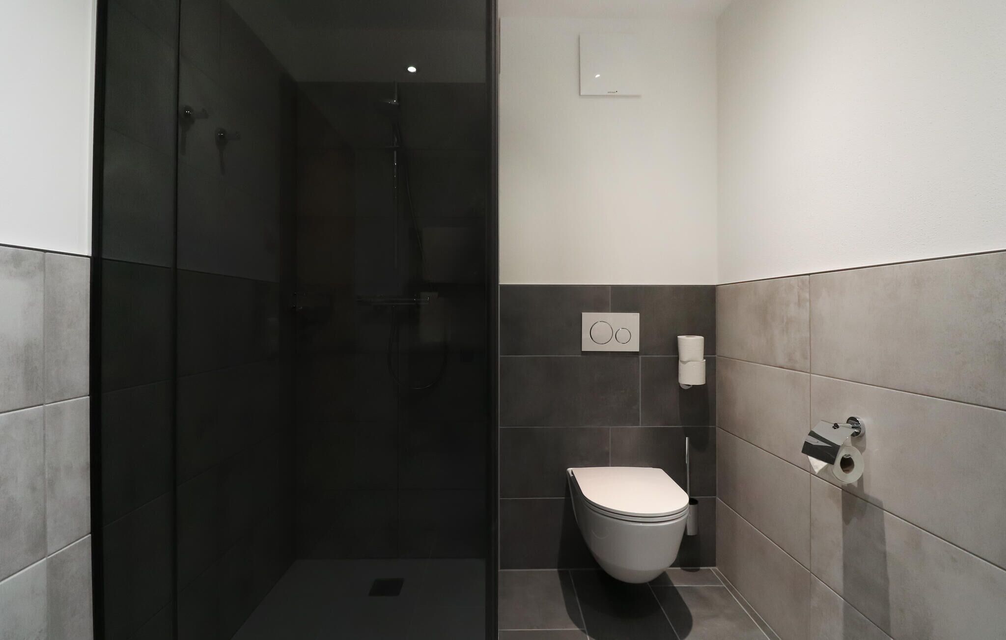 Une salle de bain moderne avec une douche à parois de verre, des toilettes et un porte-rouleau de papier toilette fixé au mur.