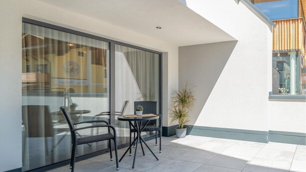 A balcony with two wicker chairs and a small table, a potted plant, and a glass door leading to an interior space. - Moderne Ferienwohnung (Großarl)