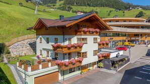 A multi-story building with balconies adorned with flowers, a garage, and a view of a green valley. - Moderne Ferienwohnung (Großarl)