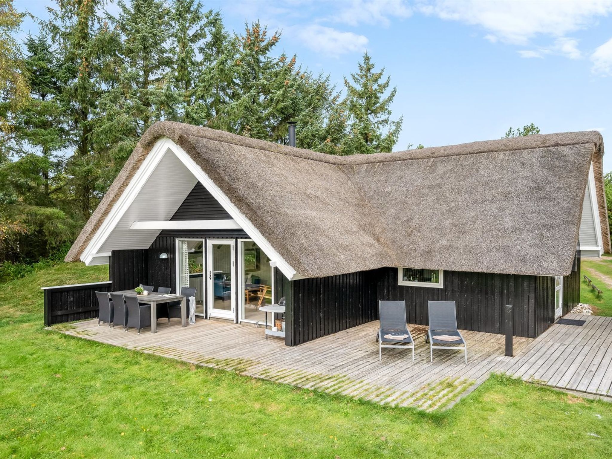 A modern house with a thatched roof, a deck with outdoor furniture, and a large window.