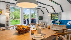 A modern interior with a dining area, a blue sofa, and a large window offering a view of the outdoors. - "Gyrial" - 2km from the sea by Interhome (Blåvand)