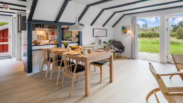 A spacious dining area with a high ceiling and exposed beams, a kitchen adjacent to the dining space, and a view of a lush garden through large windows. - "Gyrial" - 2km from the sea by Interhome (Blåvand)