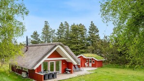 A red cabin with a thatched roof, a patio with outdoor furniture, and a grassy yard. - "Gyrial" - 2km from the sea by Interhome (Blåvand)
