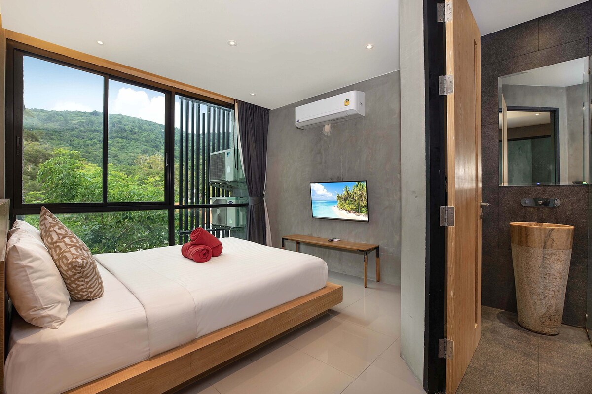 A modern hotel room with a large bed, a television, and a view of a mountainous landscape.