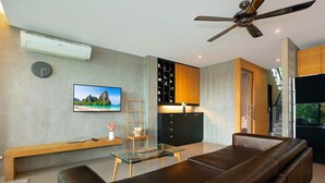 Ett modernt vardagsrum med ett soffbord i glas, en lädersoffa och en integrerad köksdel med ett svart skåp och hyllor i trä.