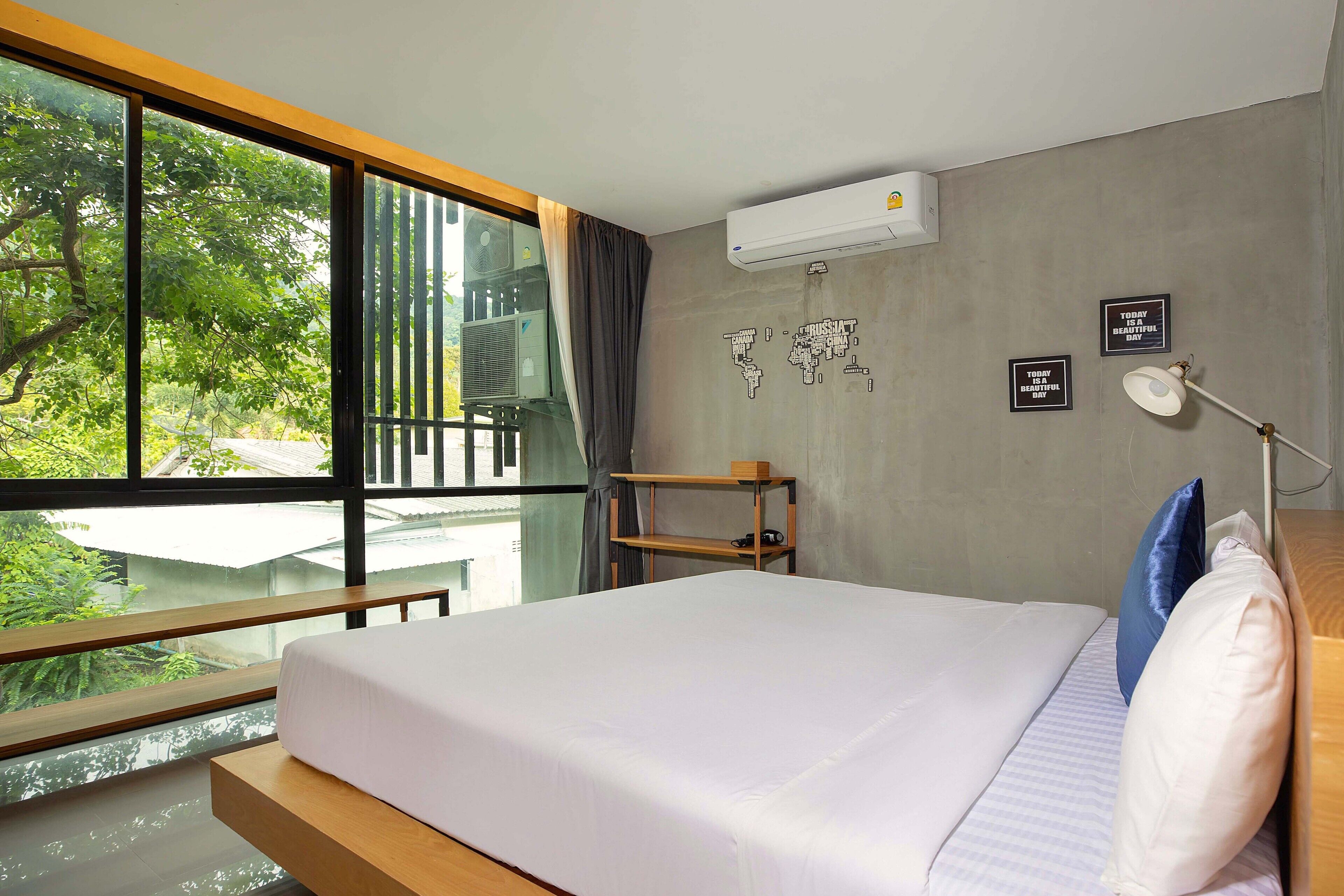 Une chambre d’hôtel avec une grande fenêtre, un lit, une table de chevet, une lampe et un appareil de climatisation.