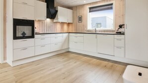 Una cocina moderna con armarios blancos, una campana extractora negra y una ventana con persianas.
