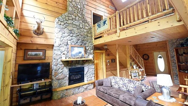 Ein Holzblockhaus mit Kamin aus Stein, einem Fernseher, einer Couch und einem Balkon.