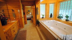 Ein Badezimmer im Holzblockhaus-Stil mit einer großen Badewanne, Holzschränken und einem Fenster mit Blick auf Grünflächen.