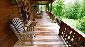 Eine hölzerne Veranda mit Adirondack-Stühlen und einem Tisch, mit Blick auf eine üppige, grüne Landschaft.