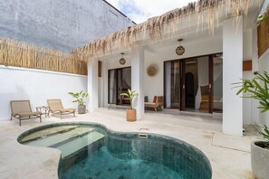 A pool area with a thatched roof, lounge chairs, and potted plants.