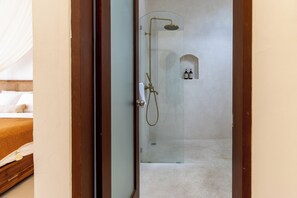 A glass-enclosed shower area with a handheld showerhead and a handheld faucet.
