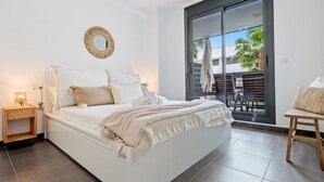 Een slaapkamer met een bed, een nachtkastje, een spiegel aan de muur en een glazen schuifdeur die uitkomt op een buitenpatio.
