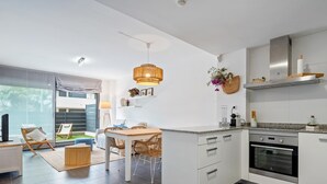Een moderne keuken met witte kastjes, een inbouwoven en een eethoek met rieten stoelen en een houten tafel.
