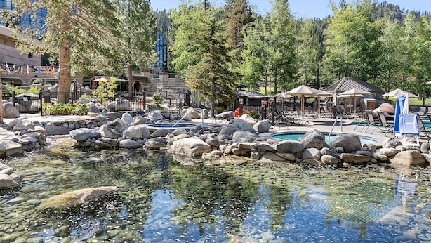 Zona de resort con piscina cristalina rodeada de rocas, sillas de descanso y un pabellón.