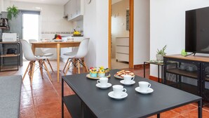 A modern kitchen with white cabinets, a dining area with a table set for breakfast, and a TV on a stand.